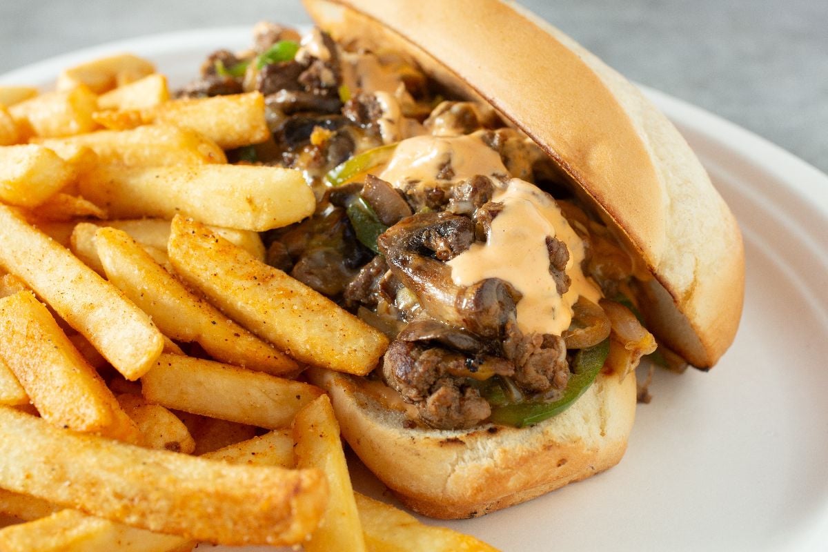 Mexican style Philly cheesesteak sandwich with fries on the side.