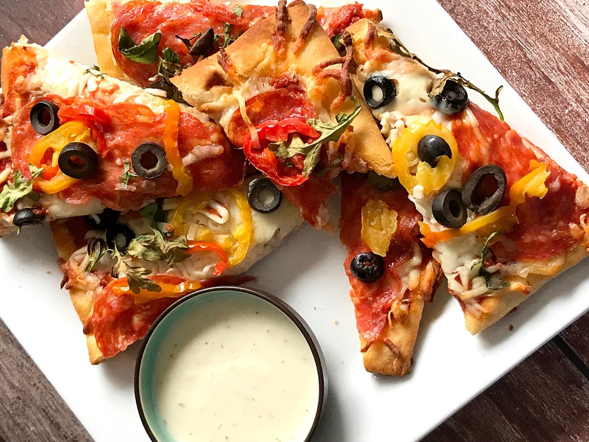 A plate of pizza with ranch dip on the side.