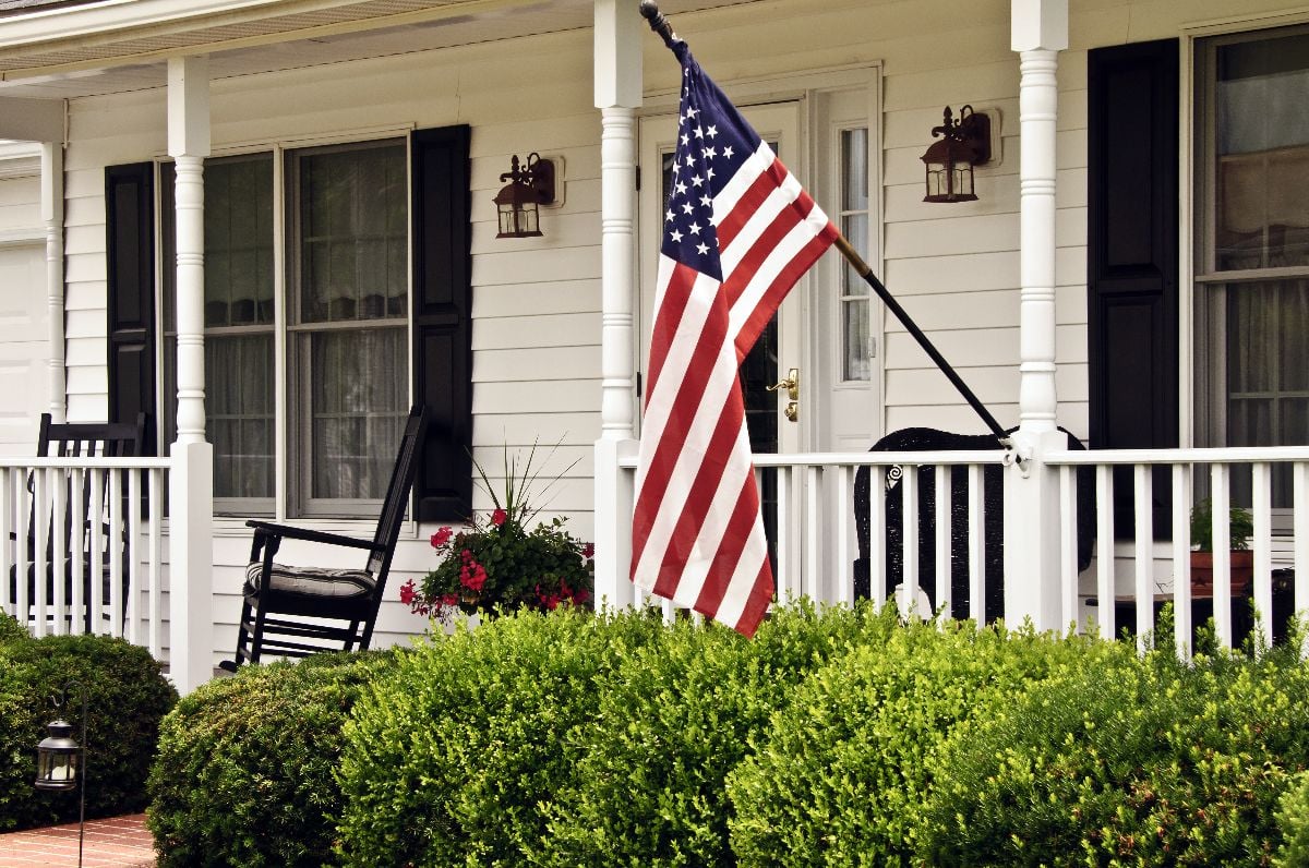 Front porch of white colonial home with American flag.