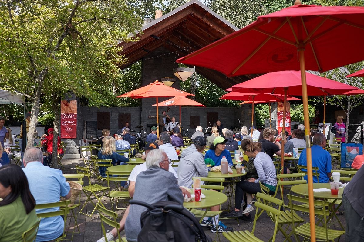 People enjoying food and live music in an outdoor seating area at the Saturday farmers market in Lake Oswego.