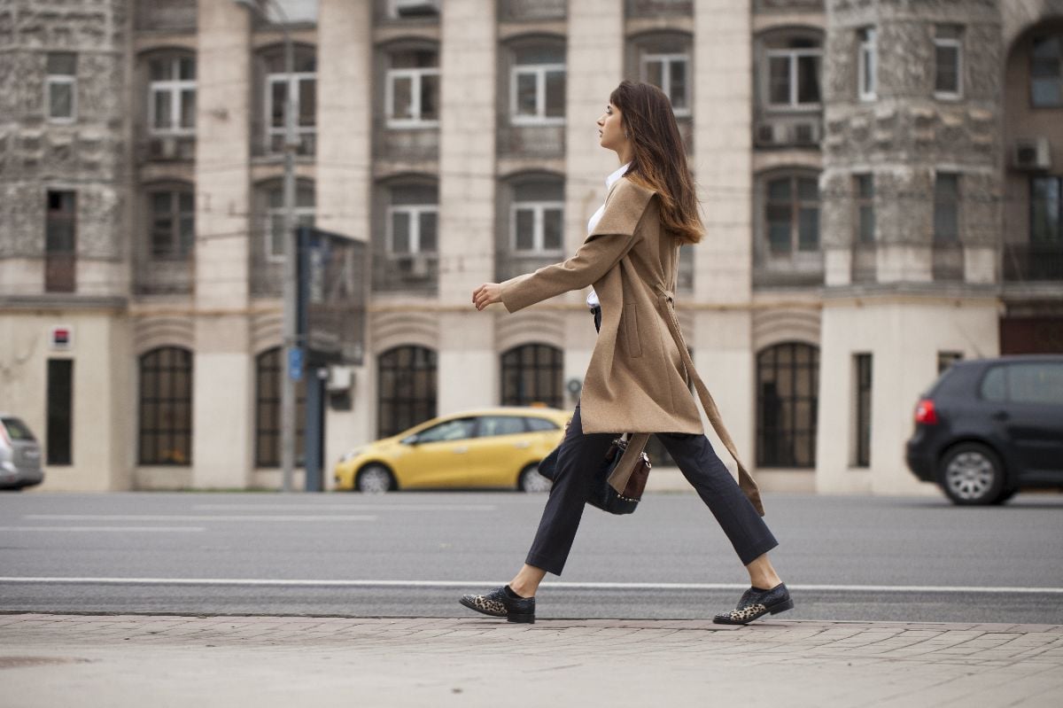 Young woman in beige coat with a bag walking on the autumn street.