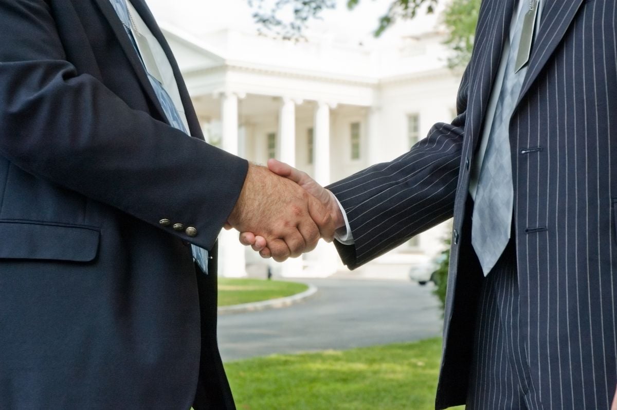 Two business men shaking hands in front of the White House in Washington DC.