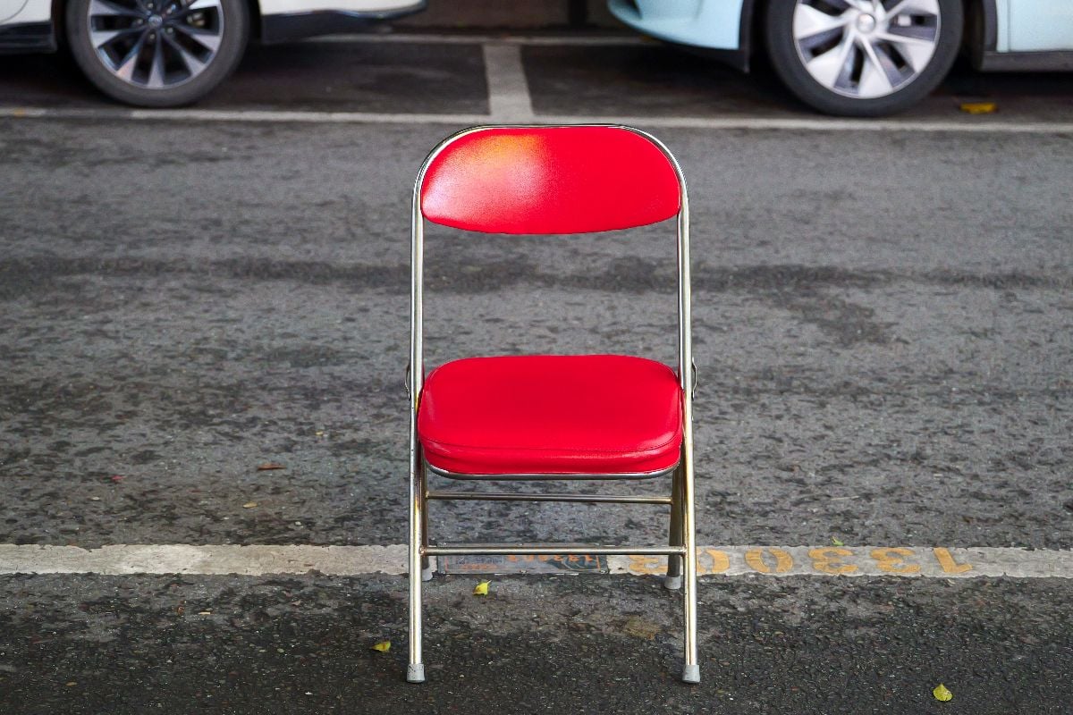 Red folding chair placed on a parking space.