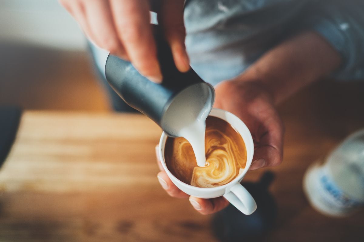 Closeup of barista hands pouring milk and preparing fresh cappuccino.