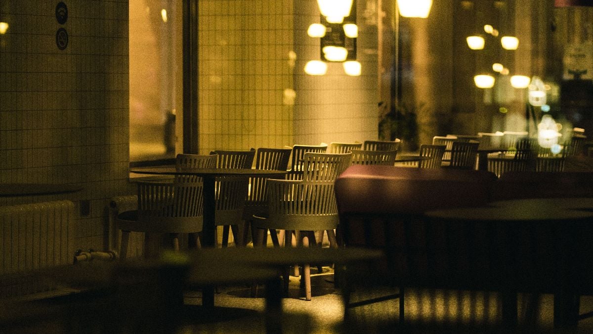 A closeup shot of tables and chairs of an empty restaurant taken from the street during night.