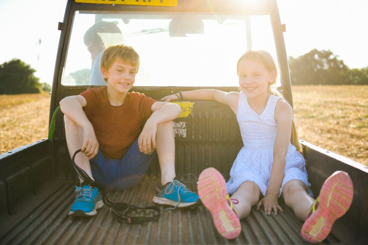 Kids sitting in the back of a truck on a farm.