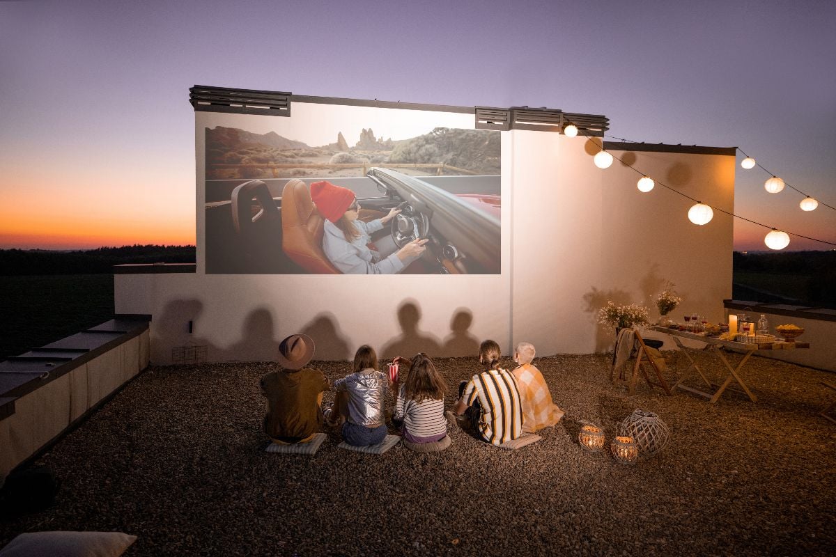 Small group of people watching movie on the rooftop terrace at sunset.