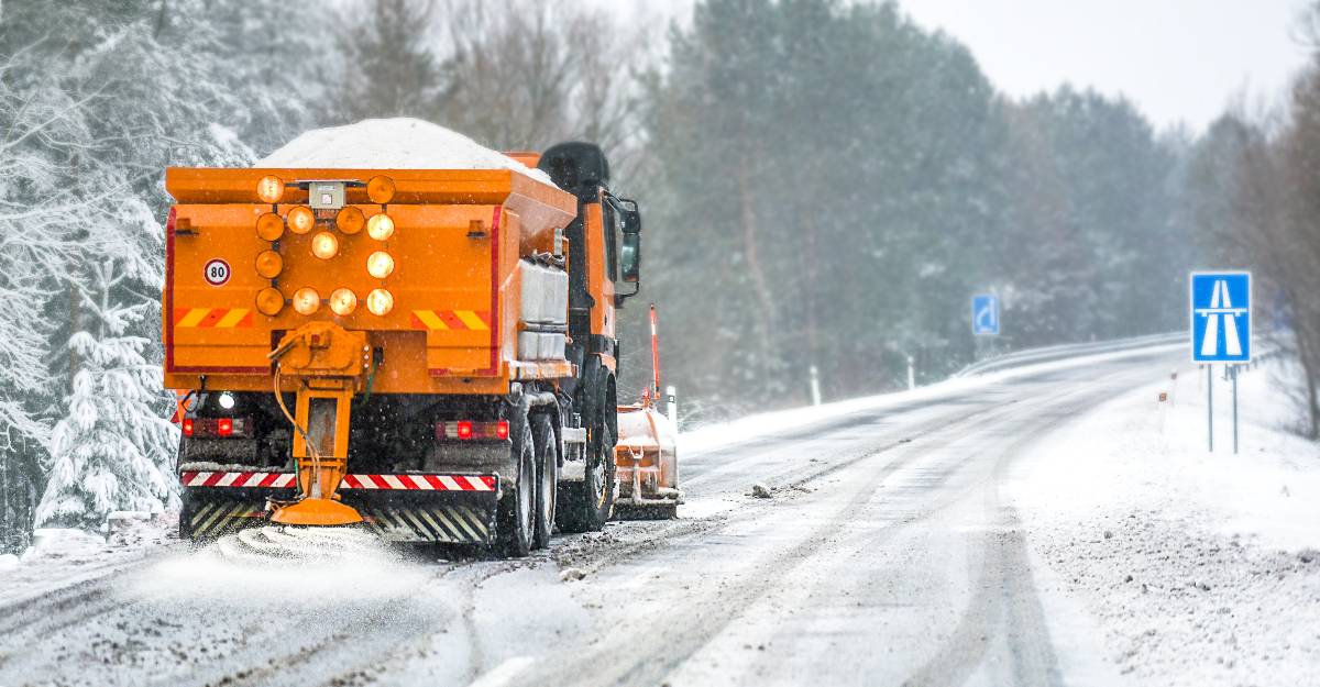 Snow plow on highway salting road.