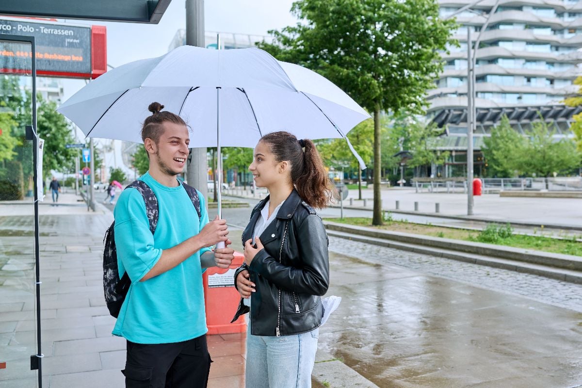 Guy sharing umbrella to girl at the bus stop.