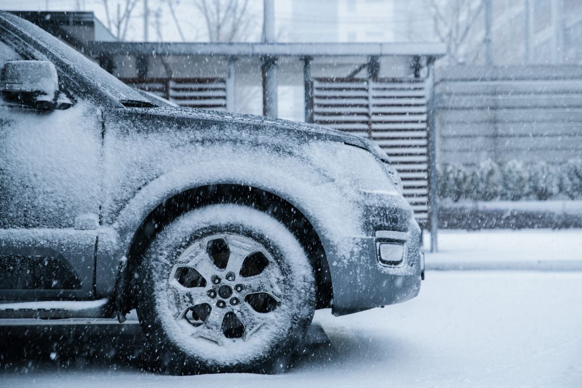 Front car wheel piled up with snow in the parking lot.