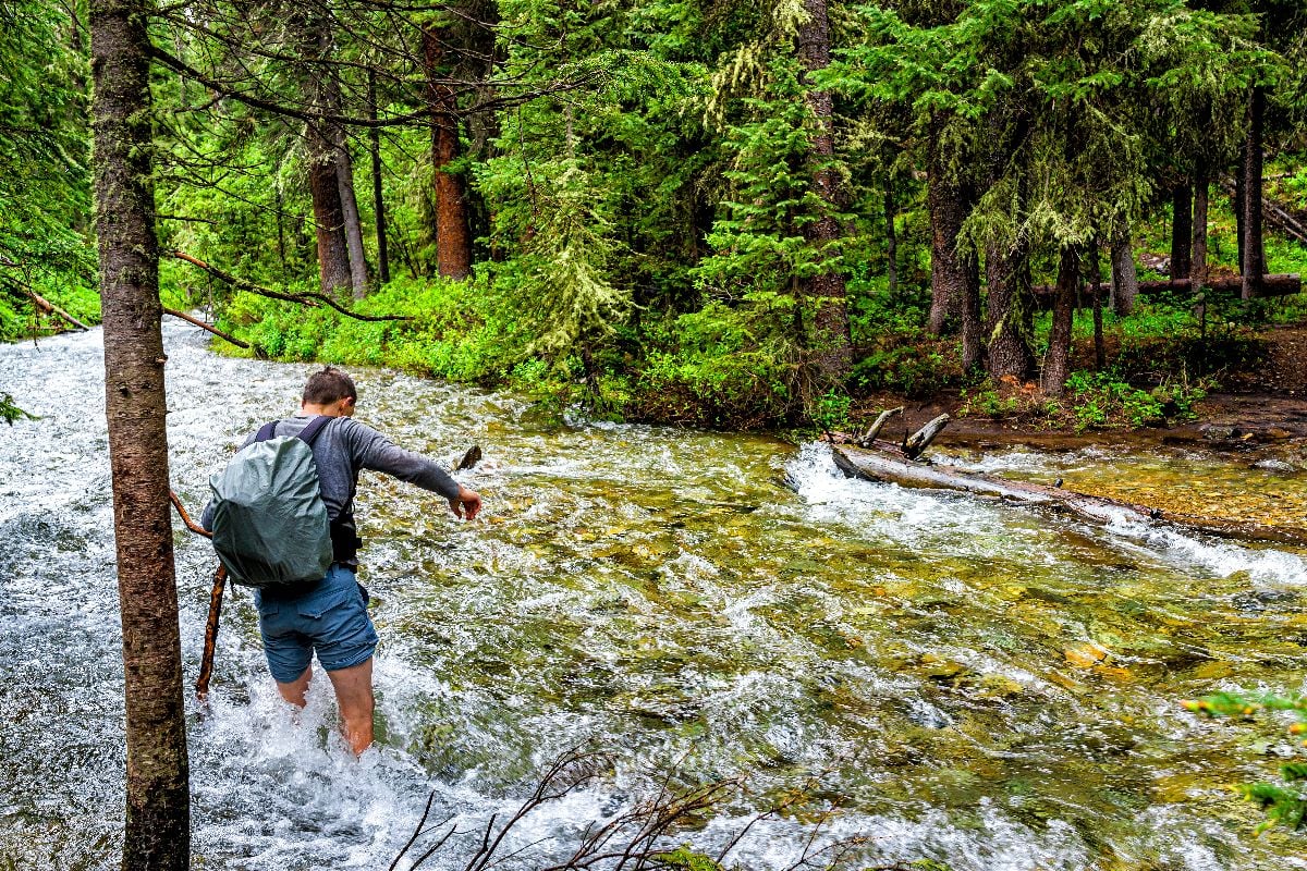 Man crossing fording river on Conundrum Creek Trail in Aspen, Colorado.