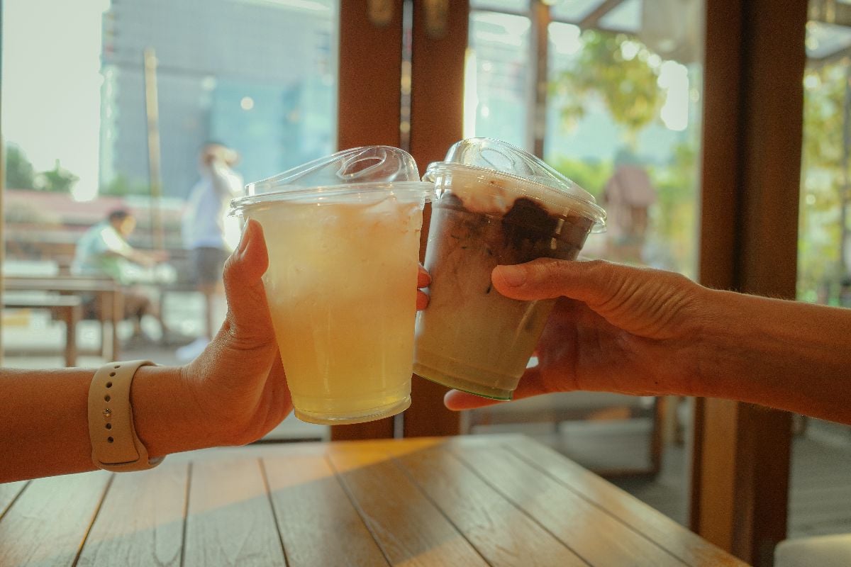 Hands holding glass of ice chocolate mint and ice mango soda together at cafe.