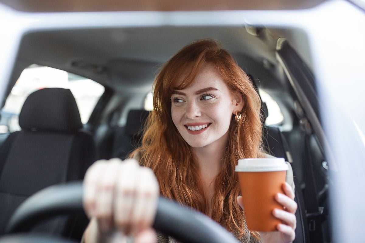 Woman with coffee to go driving her car.