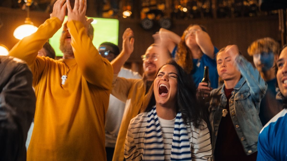 Group of soccer fans cheering their team during a football game live broadcast in a sports pub. 