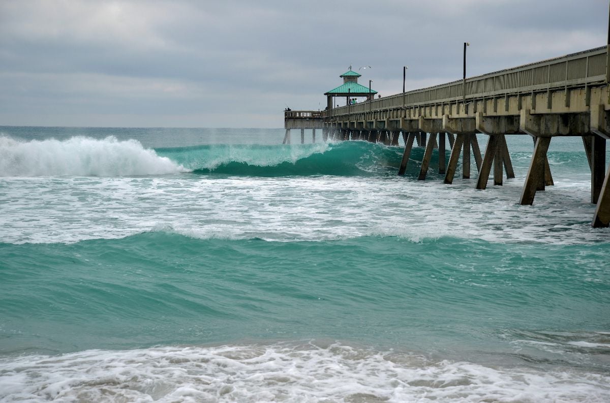 Wooden fishing pier with beach and waves crashing into surf.
