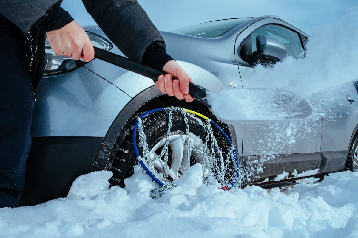 Man digs with a shovel car stuck in deep snow on winter day.