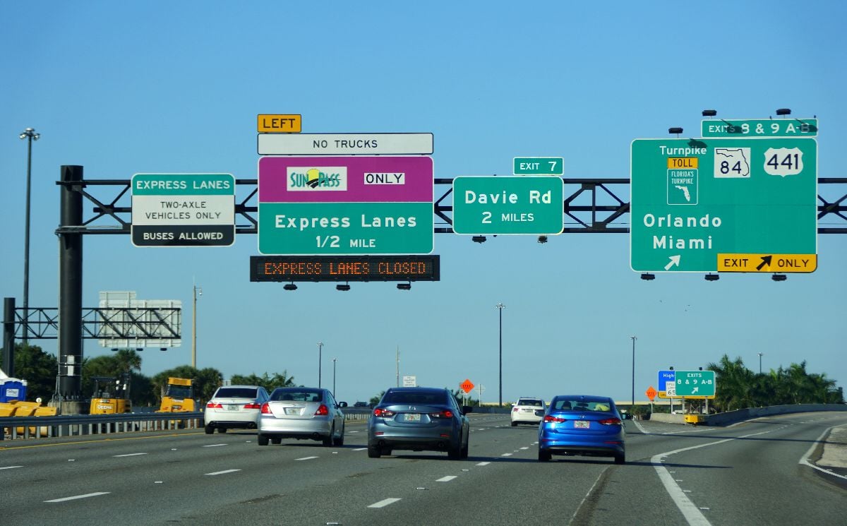 The view of four-lane traffic on 95 North with signs into Sunpass toll and Florida Turnpike into Orlando and Miami.