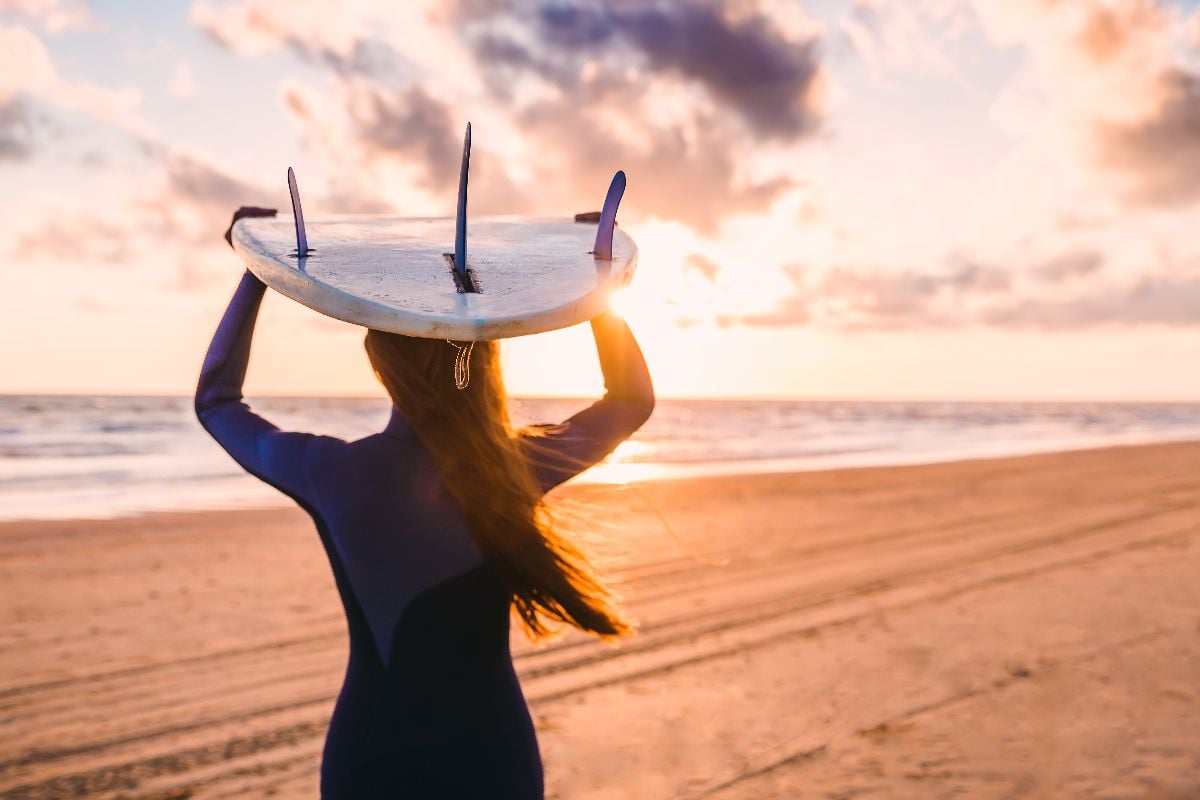 Woman holding surfboard on a beach at sunrise.