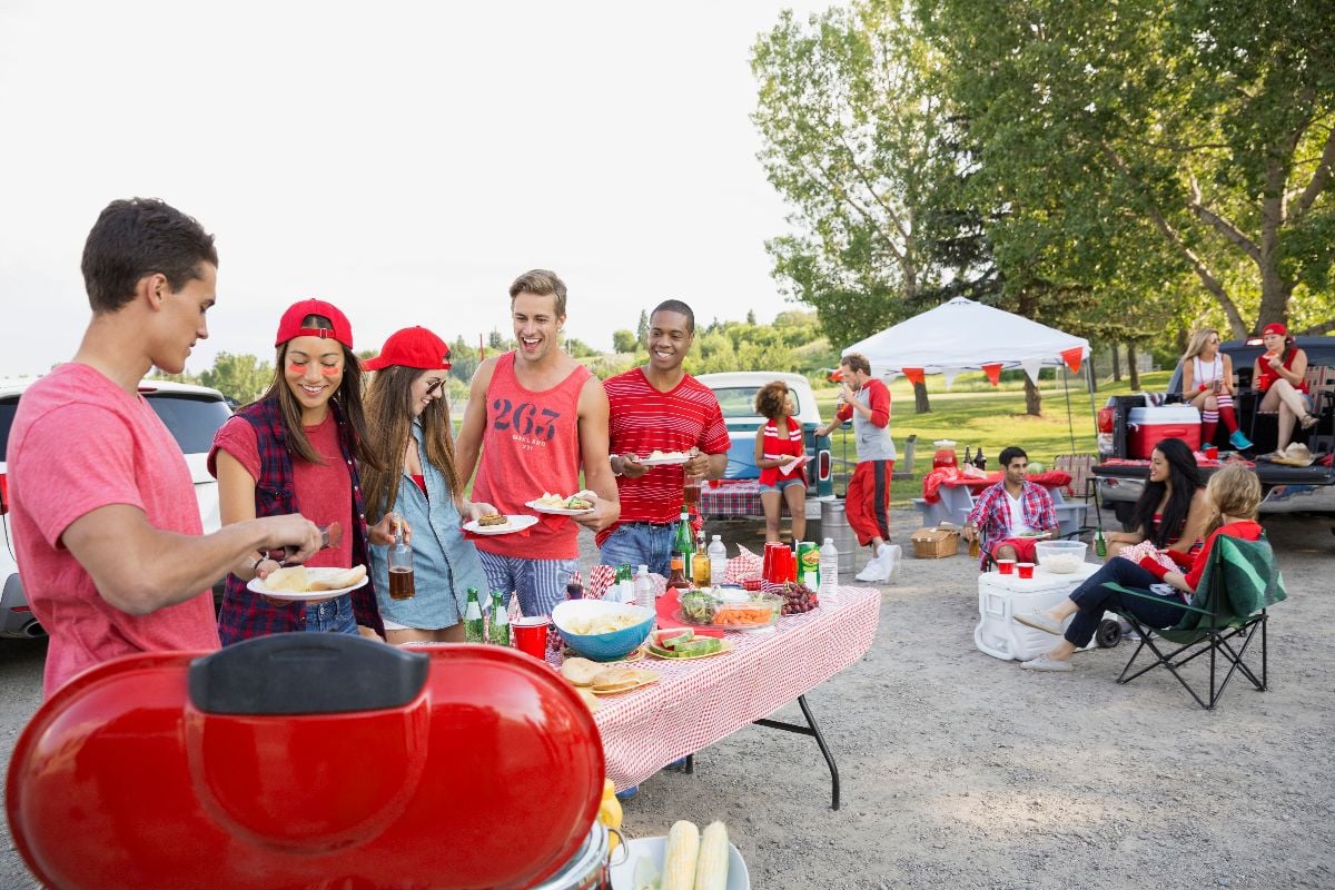 Friends eating at tailgate barbecue in field.