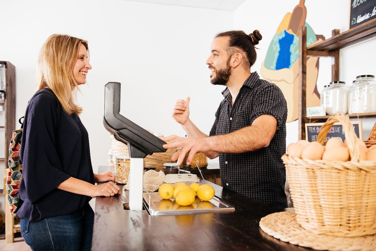Woman chats with storekeeper across a grocery counter.