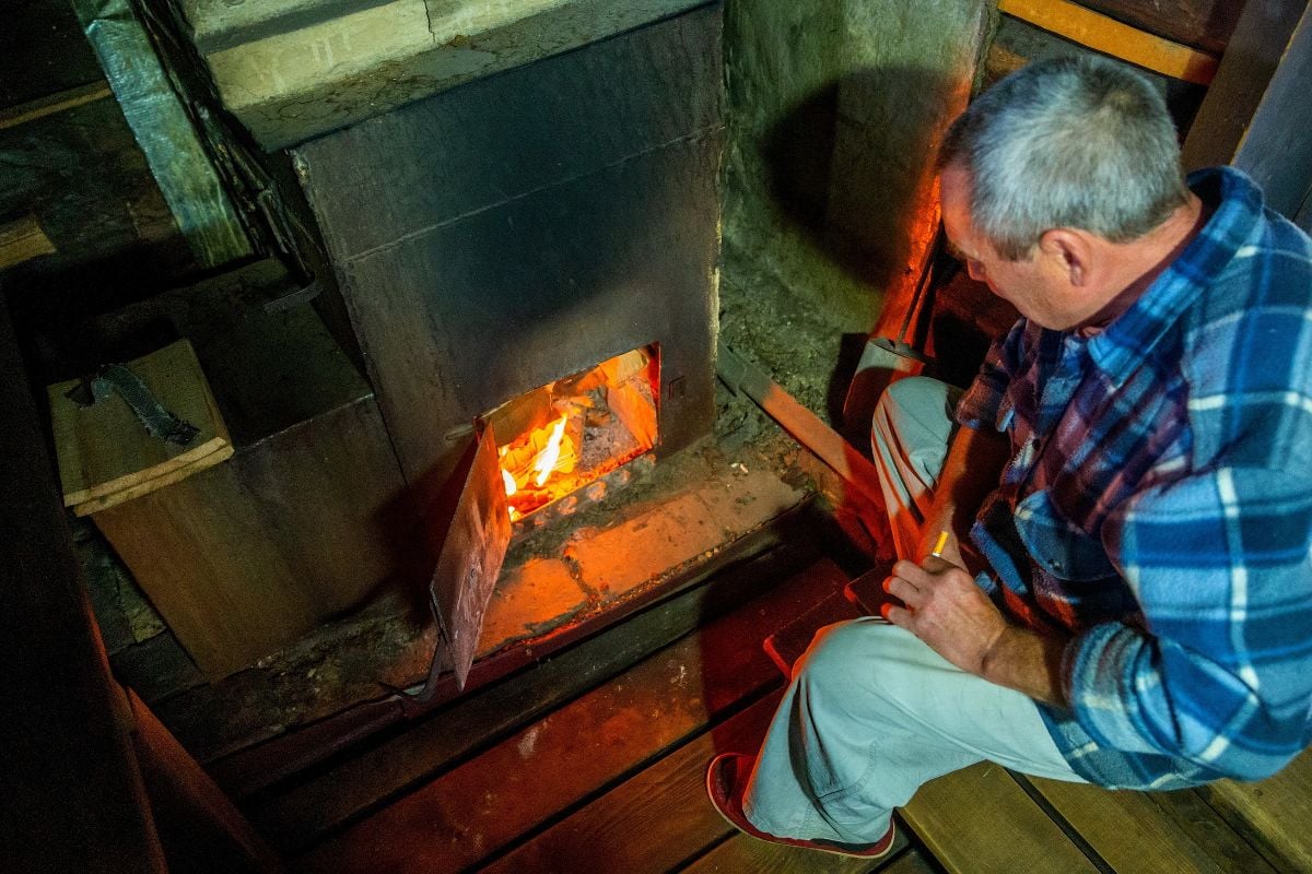 Old man tending fireplace.