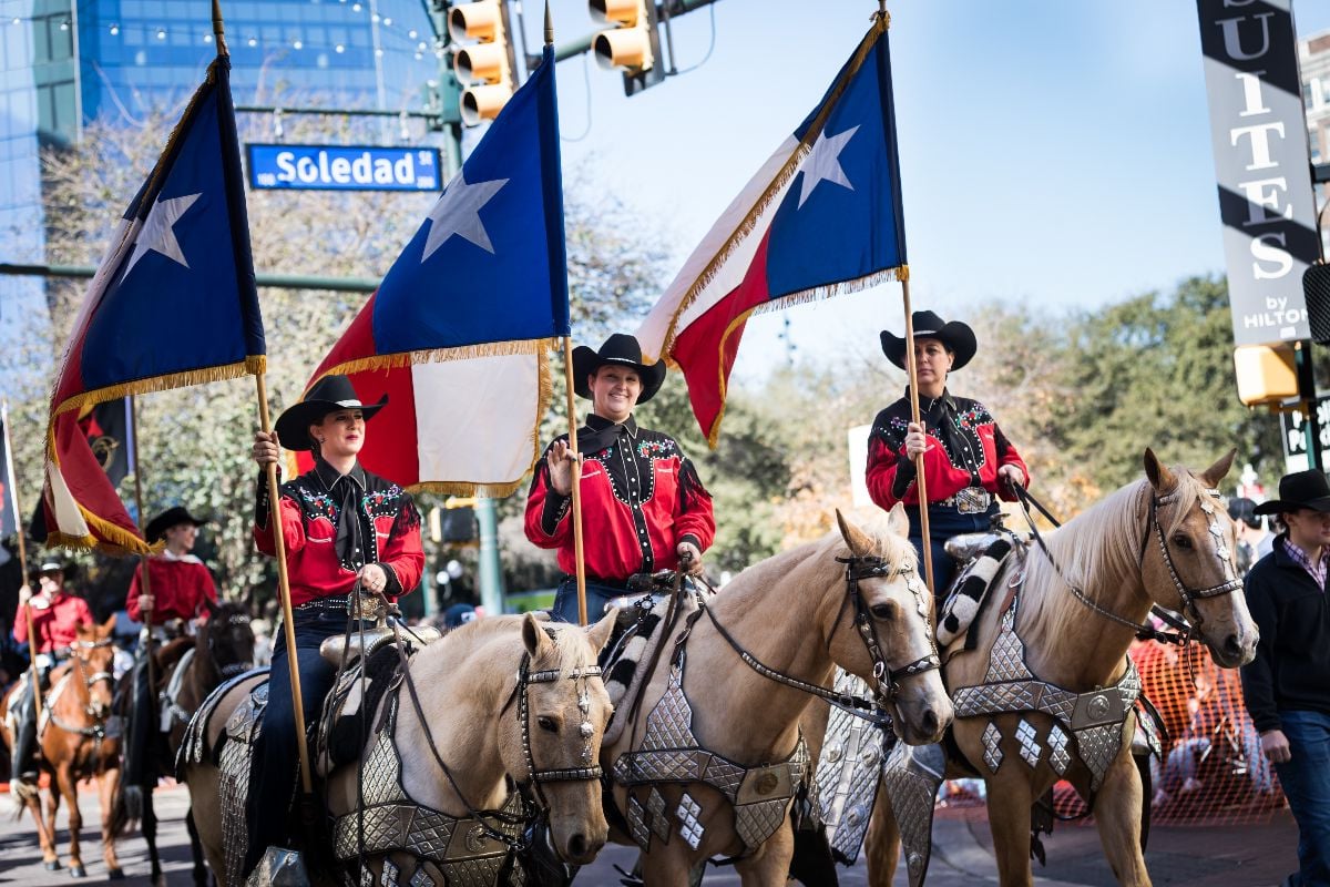 Women on horseback holding the Texas flag.