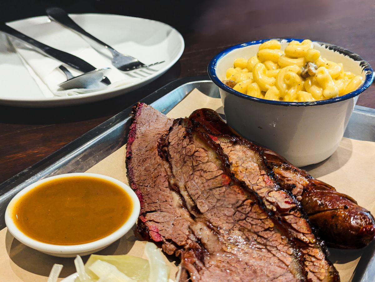 A smoked beef platter with tender brisket slices, barbecue sauce, macaroni and cheese served in big portions.