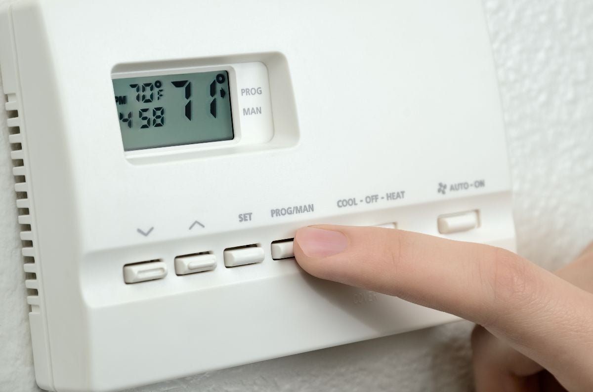 Finger pressing button on digital thermostat.