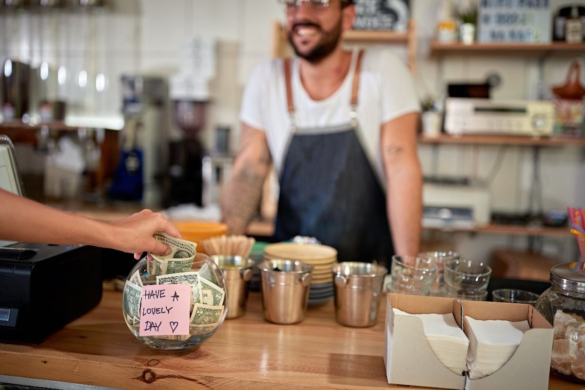 Satisfied customer in coffee shop leaving tip in a bowl.