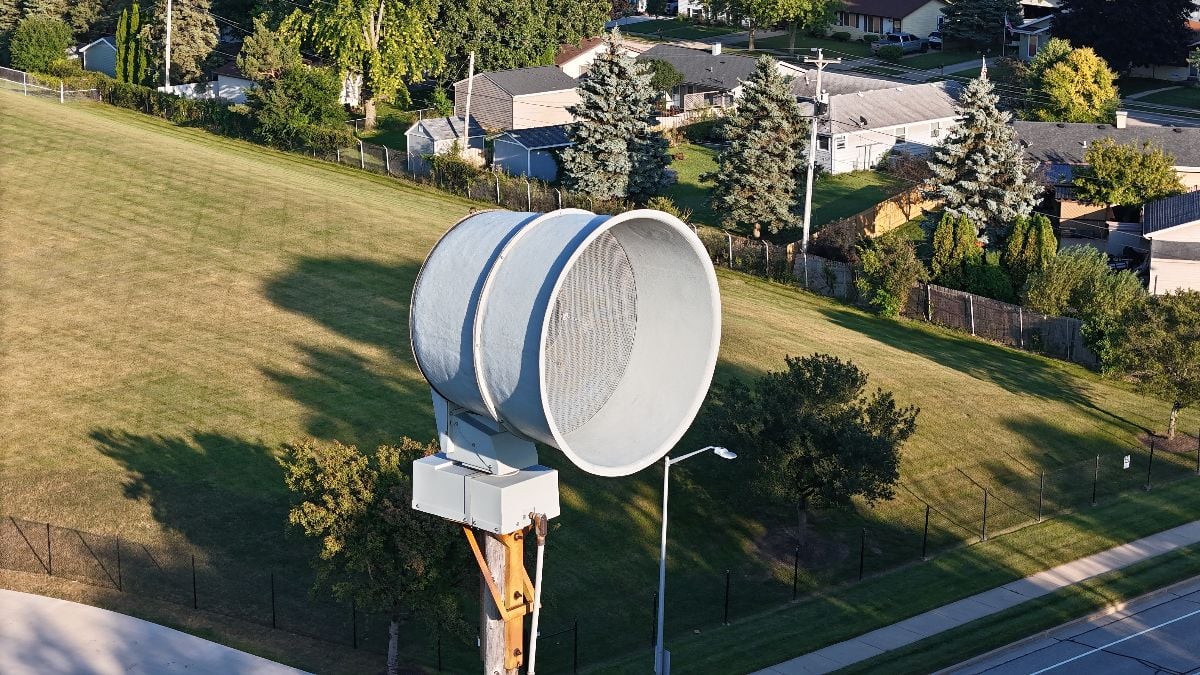 Tornado warning siren aerial view with road and field backdrop.