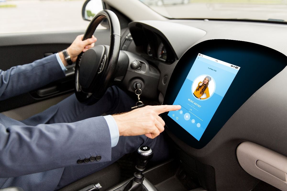 Man driving car with music player on dashboard.