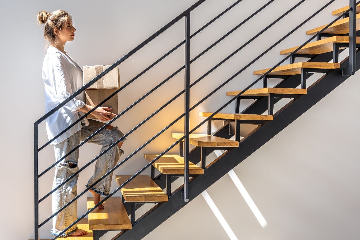 Woman with boxes walking up stairs at apartment.