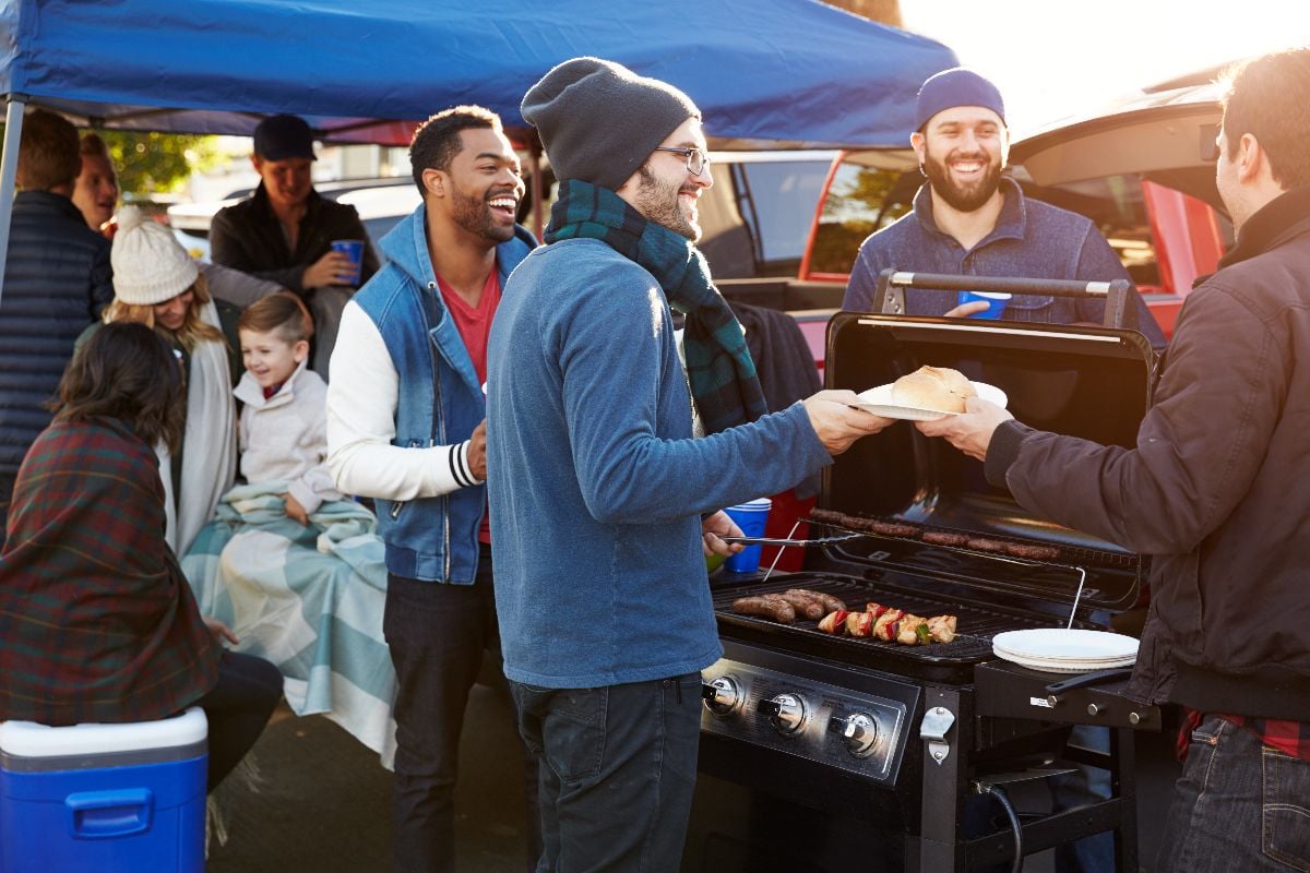 Group of sports fans tailgating in stadium car park.