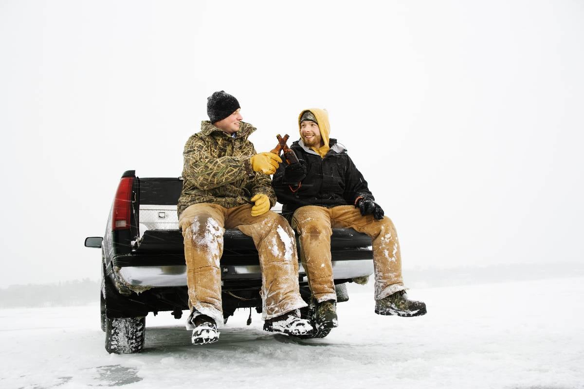 Two men enjoy a beer while sitting on the tailgate of a truck.