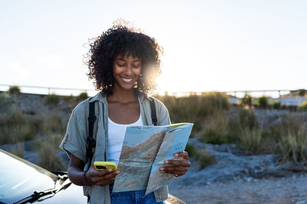 Woman holding a map and a phone outdoors.