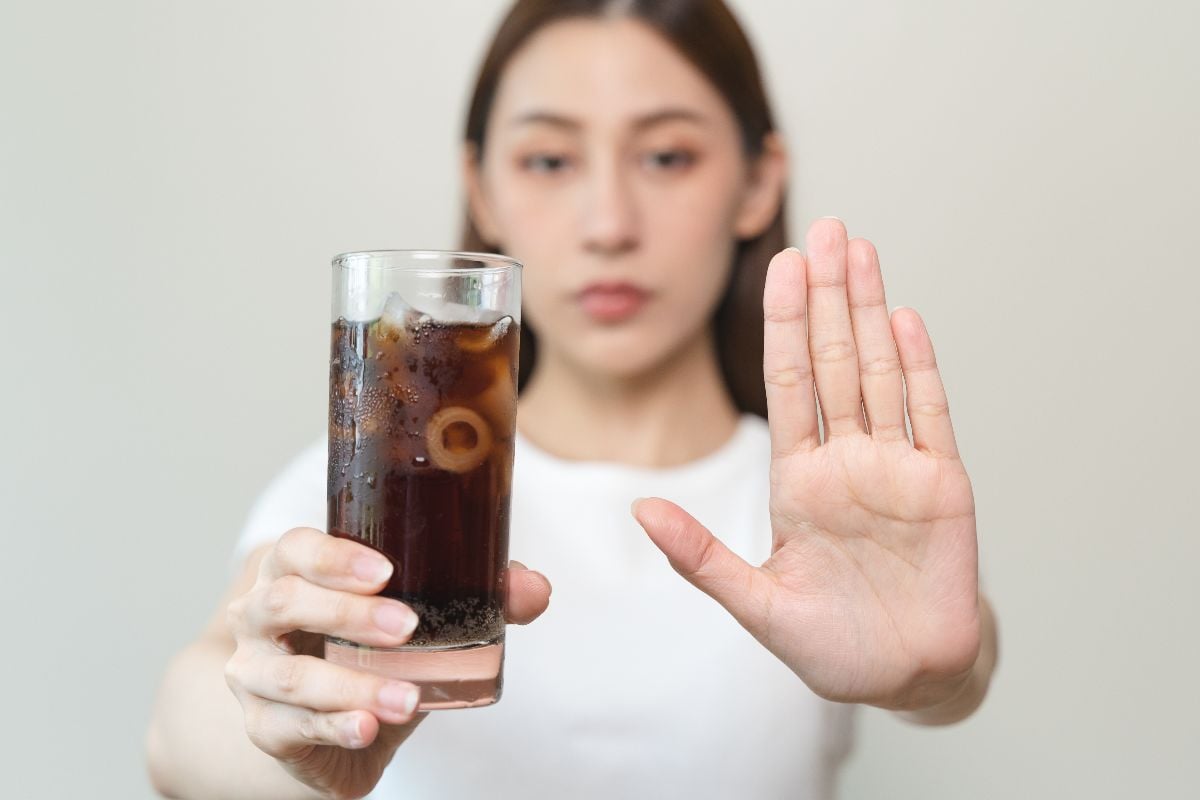 Woman holding a soda with her other hand signing stop.