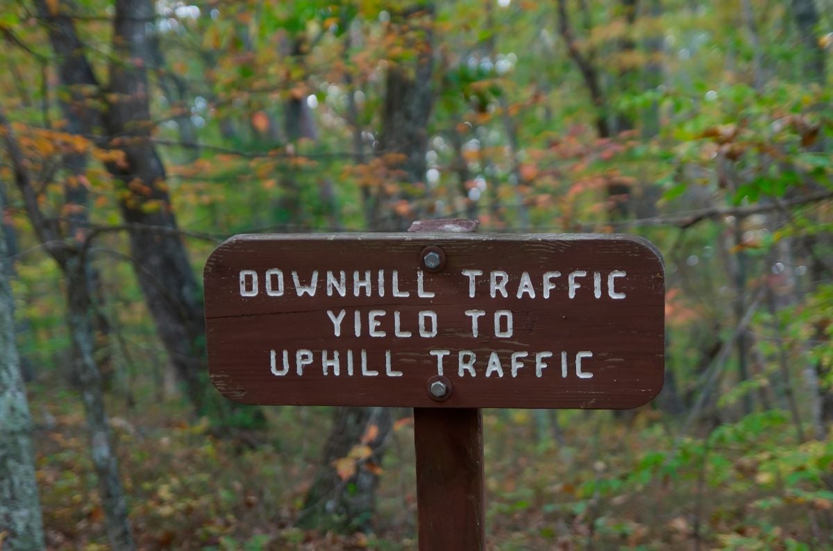 Outdoor carved wood sign that says "Downhill Traffic Yield to Uphill Traffic".
