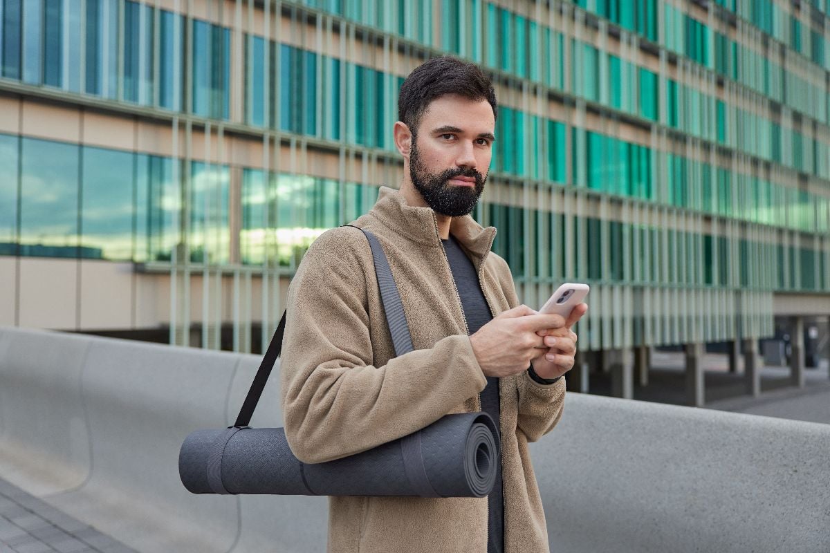 man carrying yoga mat outdoors.