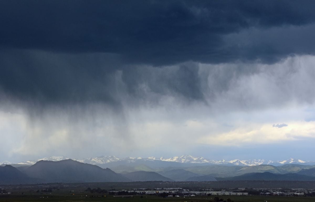 Looking out at prairie and the virga clouds of an afternoon thunderstorm in the snow-capped peaks of the front range of the Colorado rocky mountains.