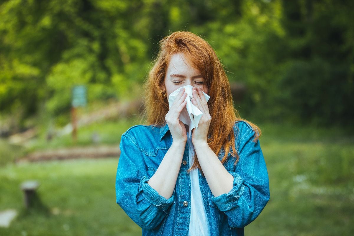 Woman blowing nose in front of blooming tree.