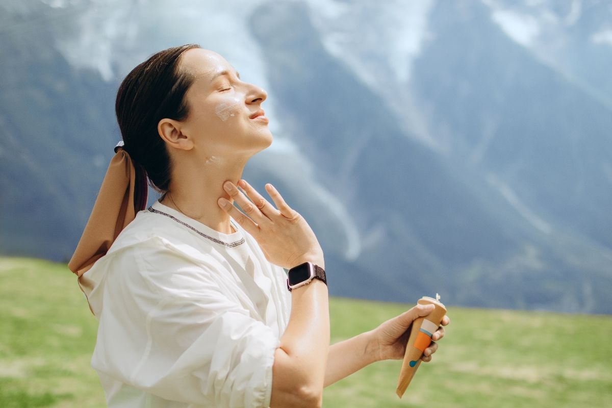 Woman applying sunscreen on her face against the mountain view.