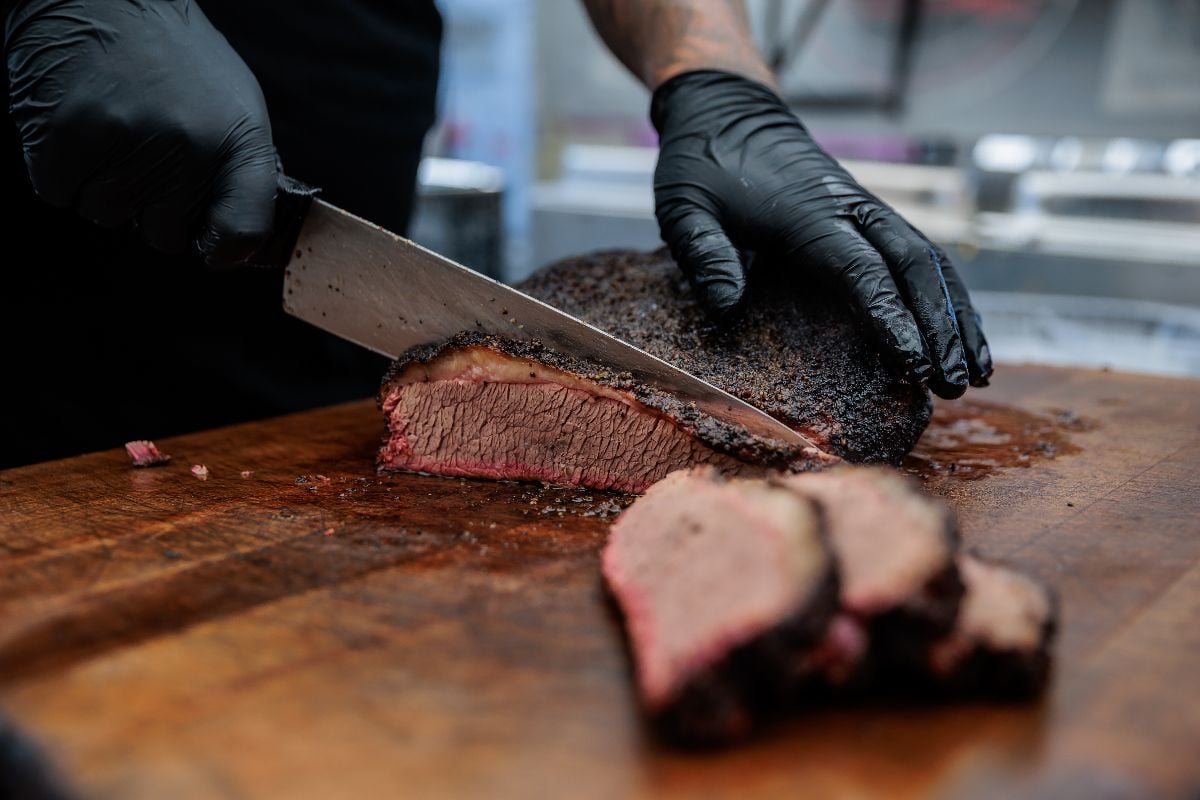 A close-up shot of a pitmaster cleanly slicing through the tender cut of beef brisket.