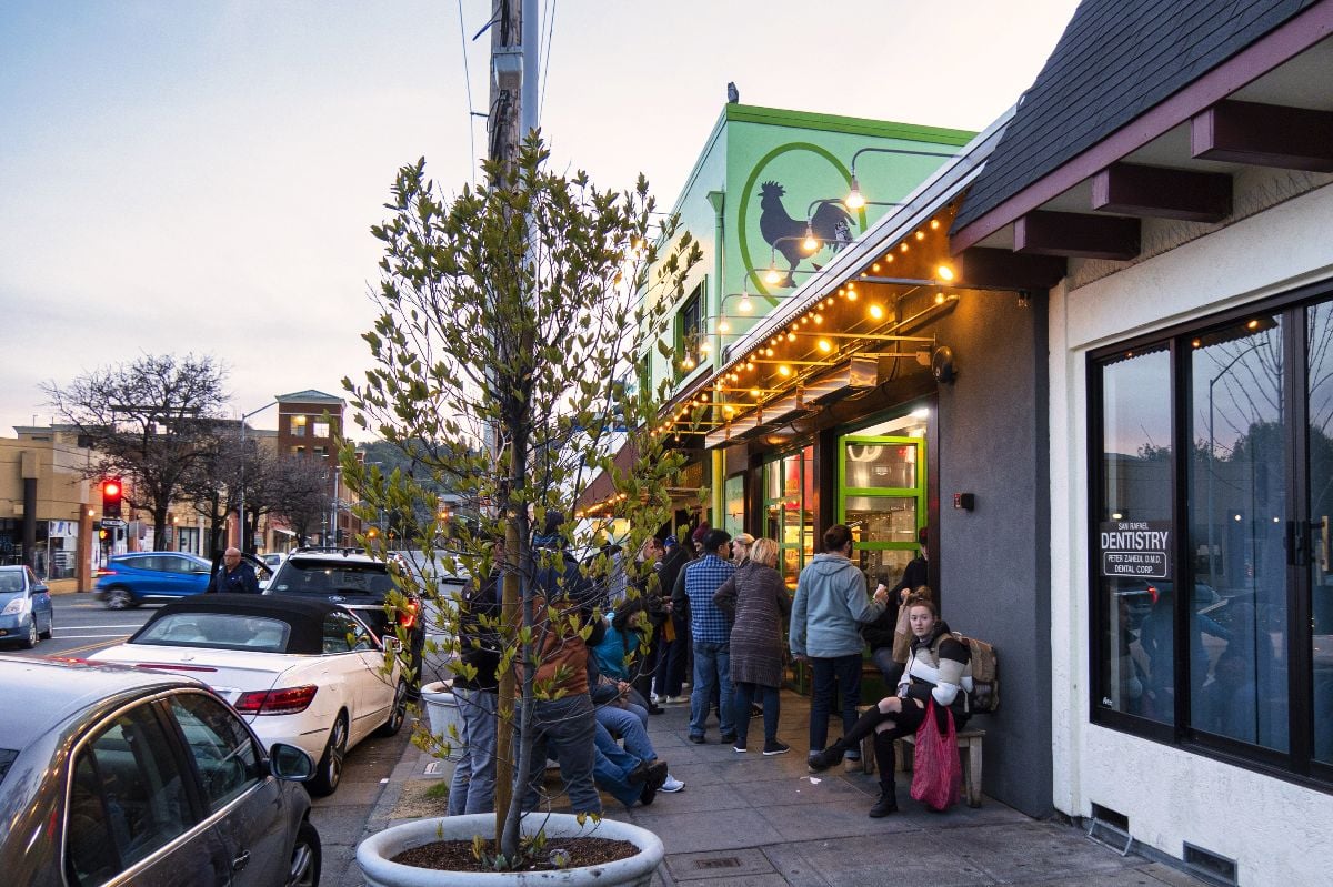 Ppeople are standing and sitting in line outside the restaurant.