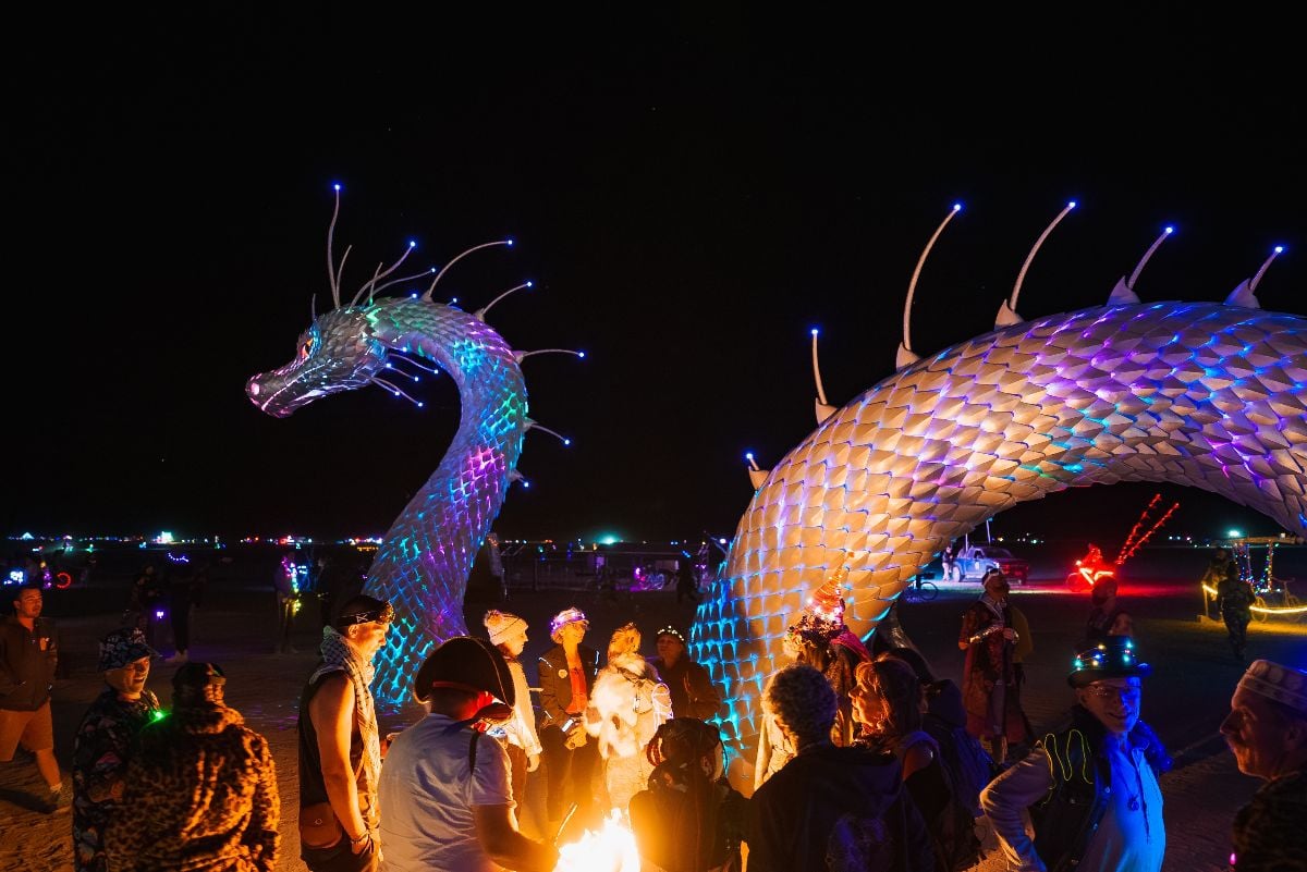 A large dragon like art installation glows with colorful lights at a Burning Man festival.