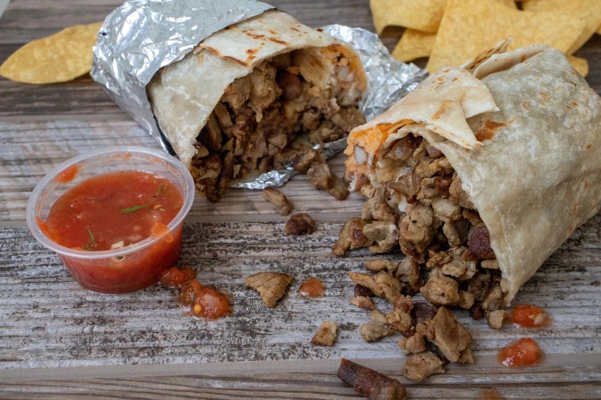 A carne asada beef burrito cut in half, accompanied with chips and salsa.