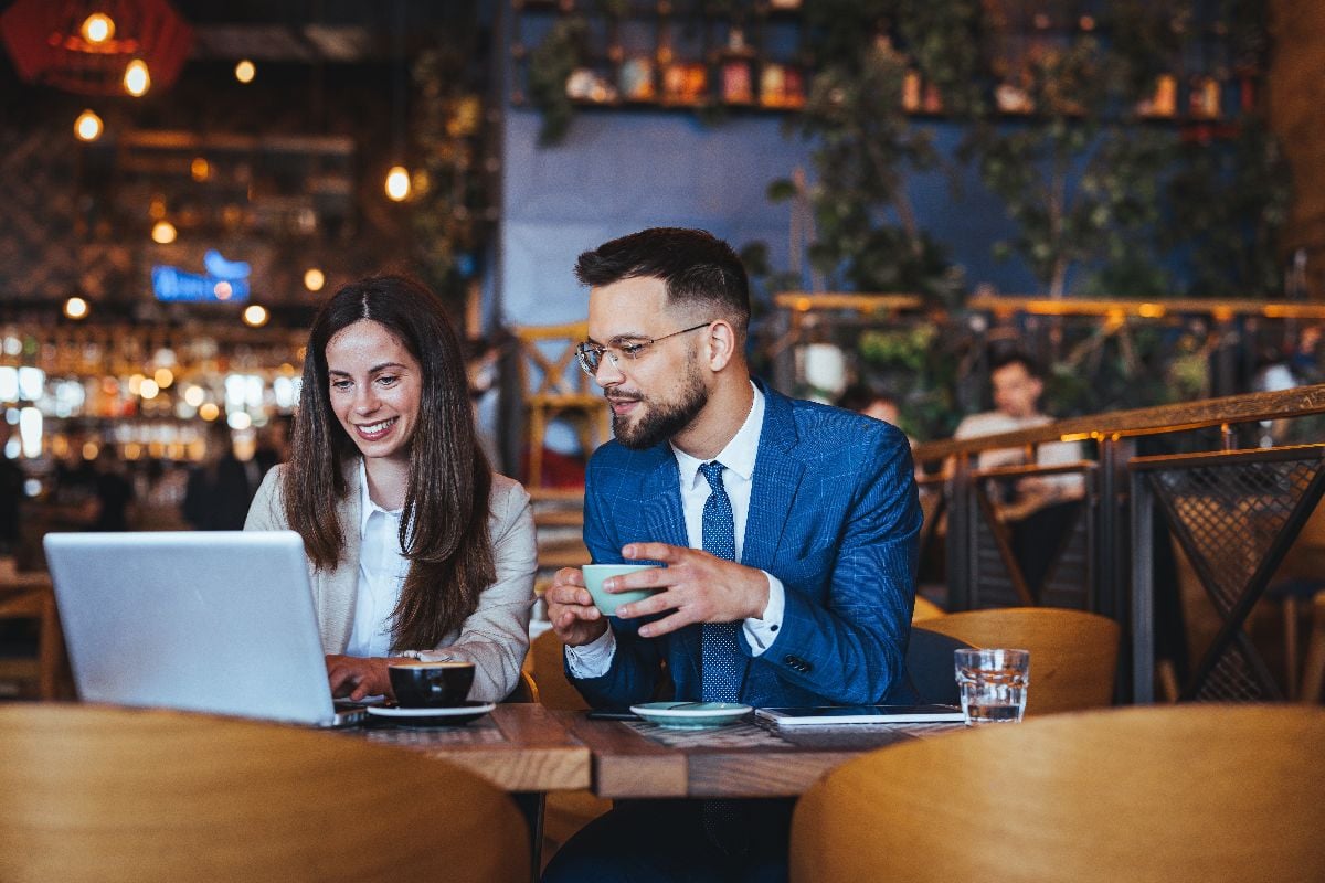Businessman and businesswoman engage in a productive meeting over a laptop in a coffee house.