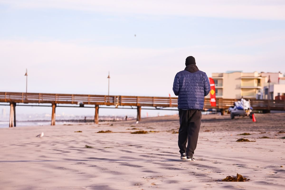 Man walking beach on cold winter morning.