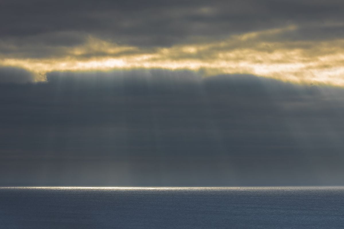 Sunbeams streaming through fog opening in the Pacific Ocean.