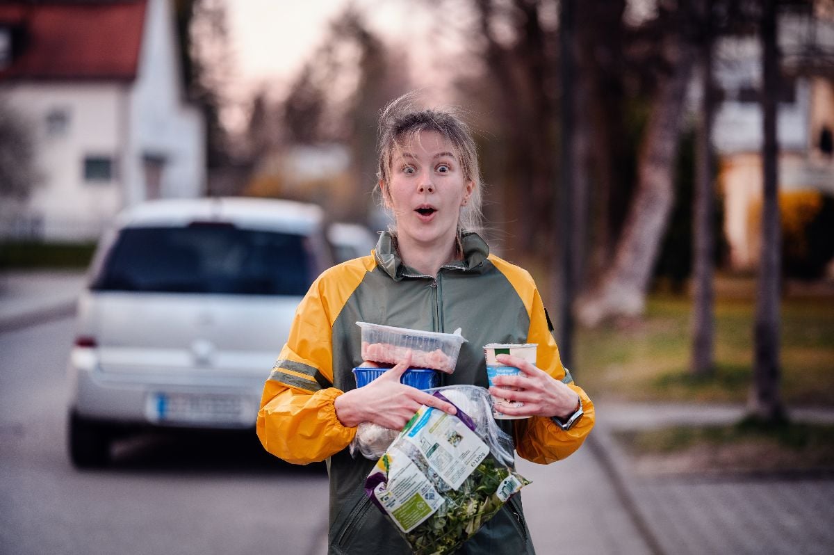 Girl standing on street with full hands of groceries.