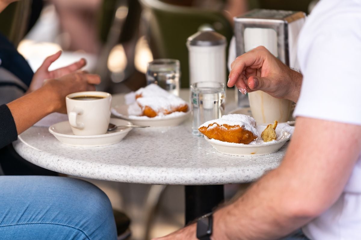 Closeup of couple drinking chicory coffee and eating deep fried beignet donut.